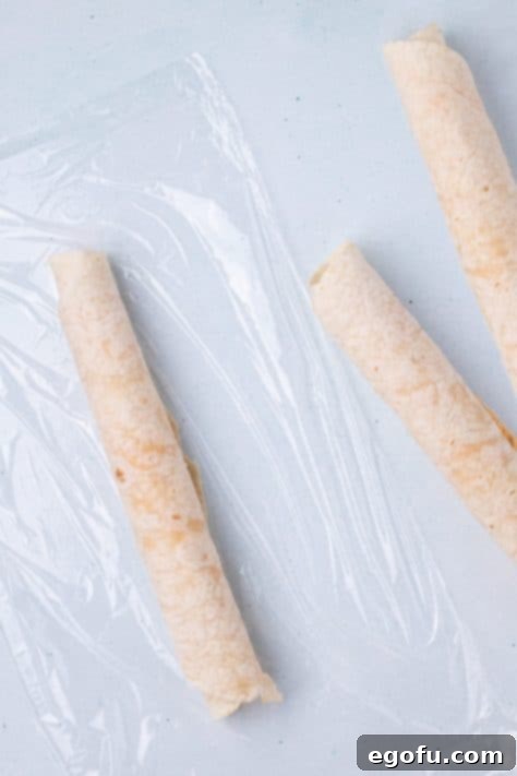 Tortillas filled with cream cheese buffalo mixture being wrapped in plastic wrap.