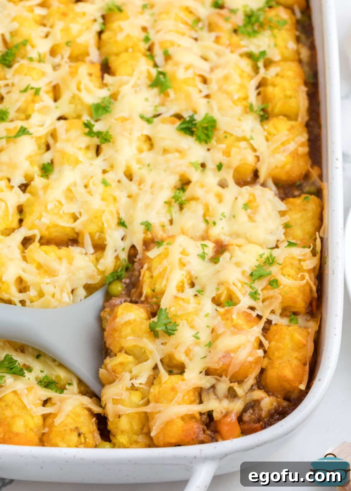 Looking down on a baking dish with a serving utensil in some Shepherd's Pie Tater Tot Casserole.