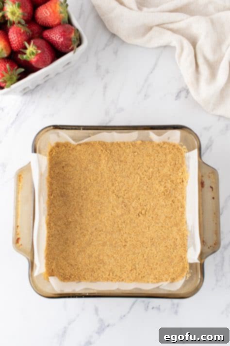 Luscious Strawberry Crumble Cheesecake Squares 7 Graham cracker crumb crust in a baking dish, perfectly pressed and ready for the next layer.