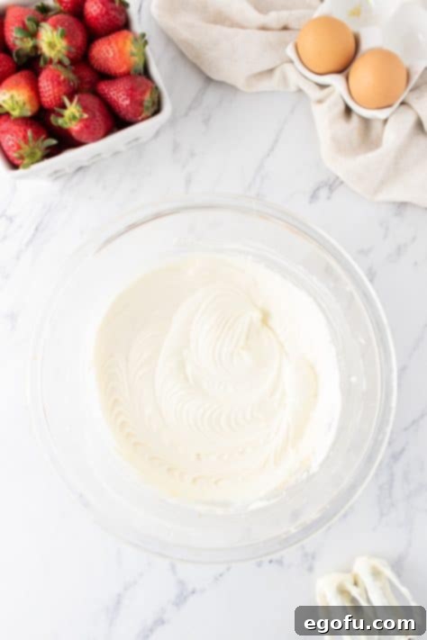 Luscious Strawberry Crumble Cheesecake Squares 8 The initial stage of the creamy cheesecake layer, showing cream cheese, sugar, vanilla extract, and Greek yogurt being mixed together in a bowl.