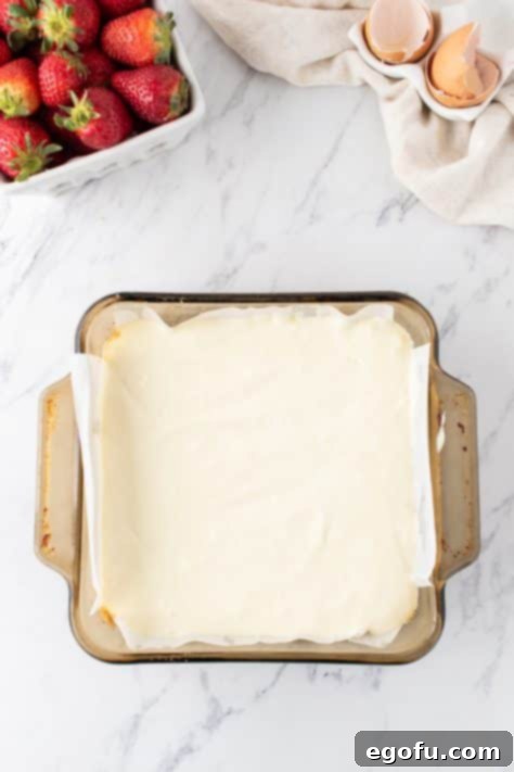 Luscious Strawberry Crumble Cheesecake Squares 9 The smooth cheesecake batter, with eggs just incorporated, being spread evenly over the pre-baked graham cracker crust in the baking pan.