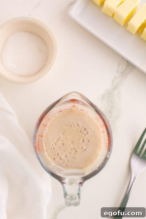 Golden Buttery Brioche Buns Fresh From Your Oven 15 A measuring cup with yeast activating, showing a foamy surface.