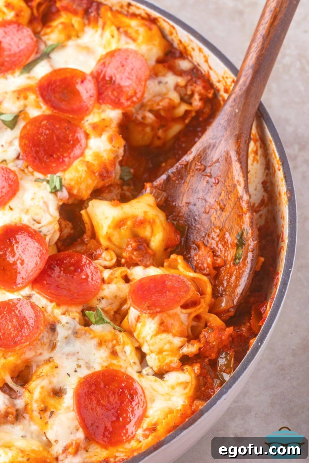 A wooden spoon in a pot of Pizza Tortellini, showcasing its rich texture and melty cheese.
