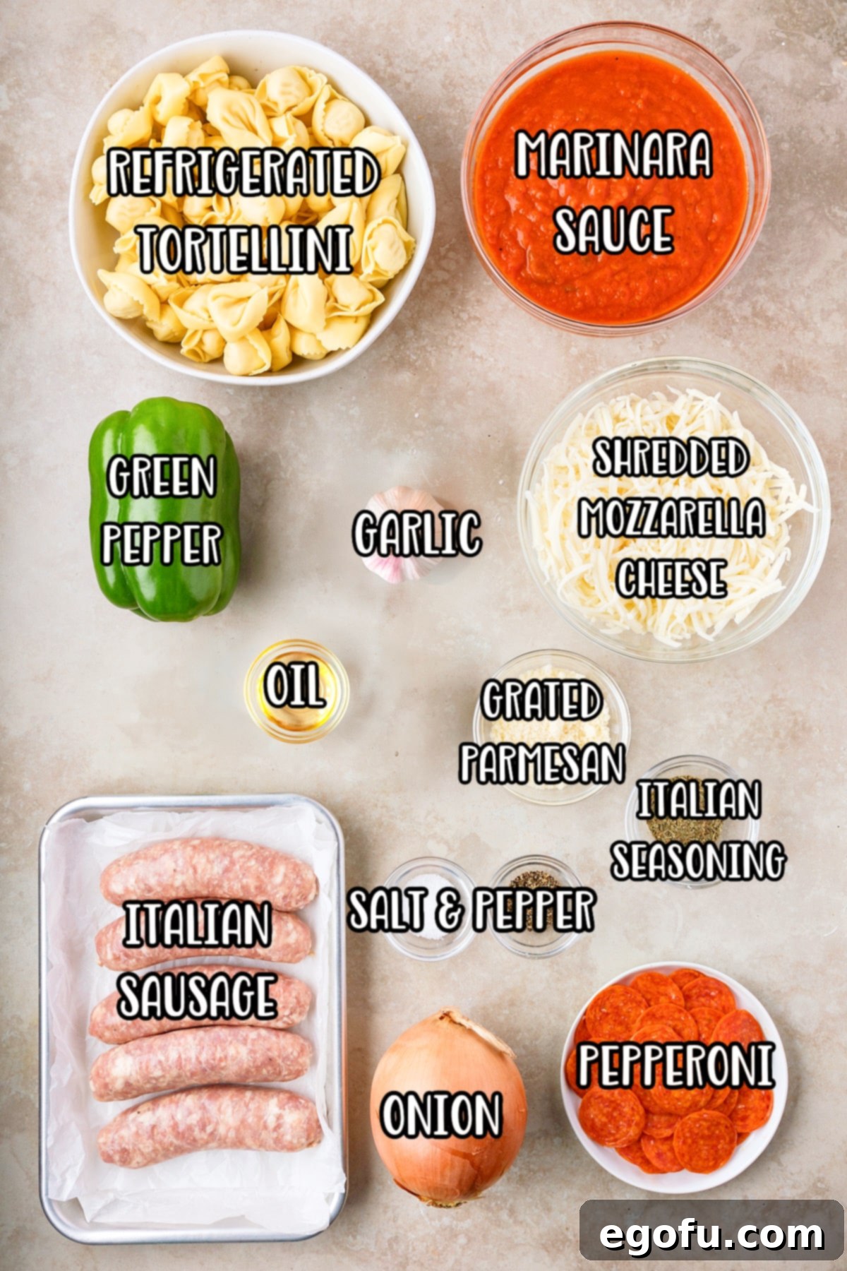 A flat lay of all the essential ingredients for Pizza Tortellini: refrigerated tortellini, marinara sauce, shredded cheese, green pepper, oil, garlic, onion, pepperoni, Italian sausage, salt, pepper, and parmesan cheese.