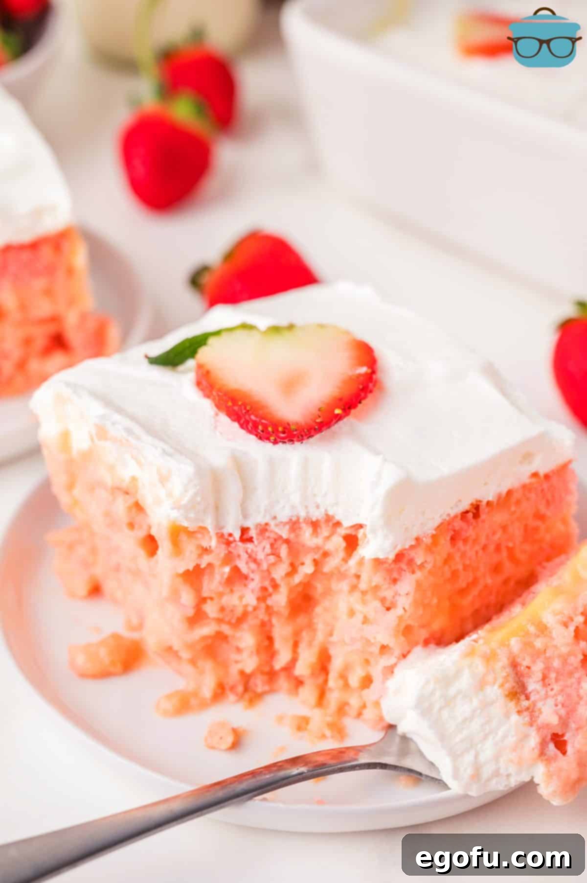 Velvety Strawberry Poke Cake Bliss 9 A fork holding a bite of Strawberry Pudding Poke cake next to a slice of it, ready to be eaten.