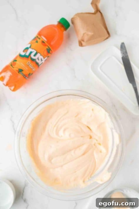 Zesty Orange Cream Pie 14 Cool Whip being added to a bowl with orange soda and pudding mix.