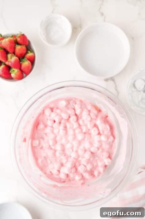 A bowl with strawberry Jell-O mix, boiling water, pineapple chunks, diced strawberries, mini marshmallows, and marshmallow creme.