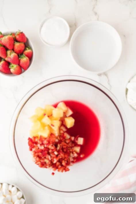 A bowl with strawberry Jell-O mix, boiling water, pineapple chunks and the diced strawberries.
