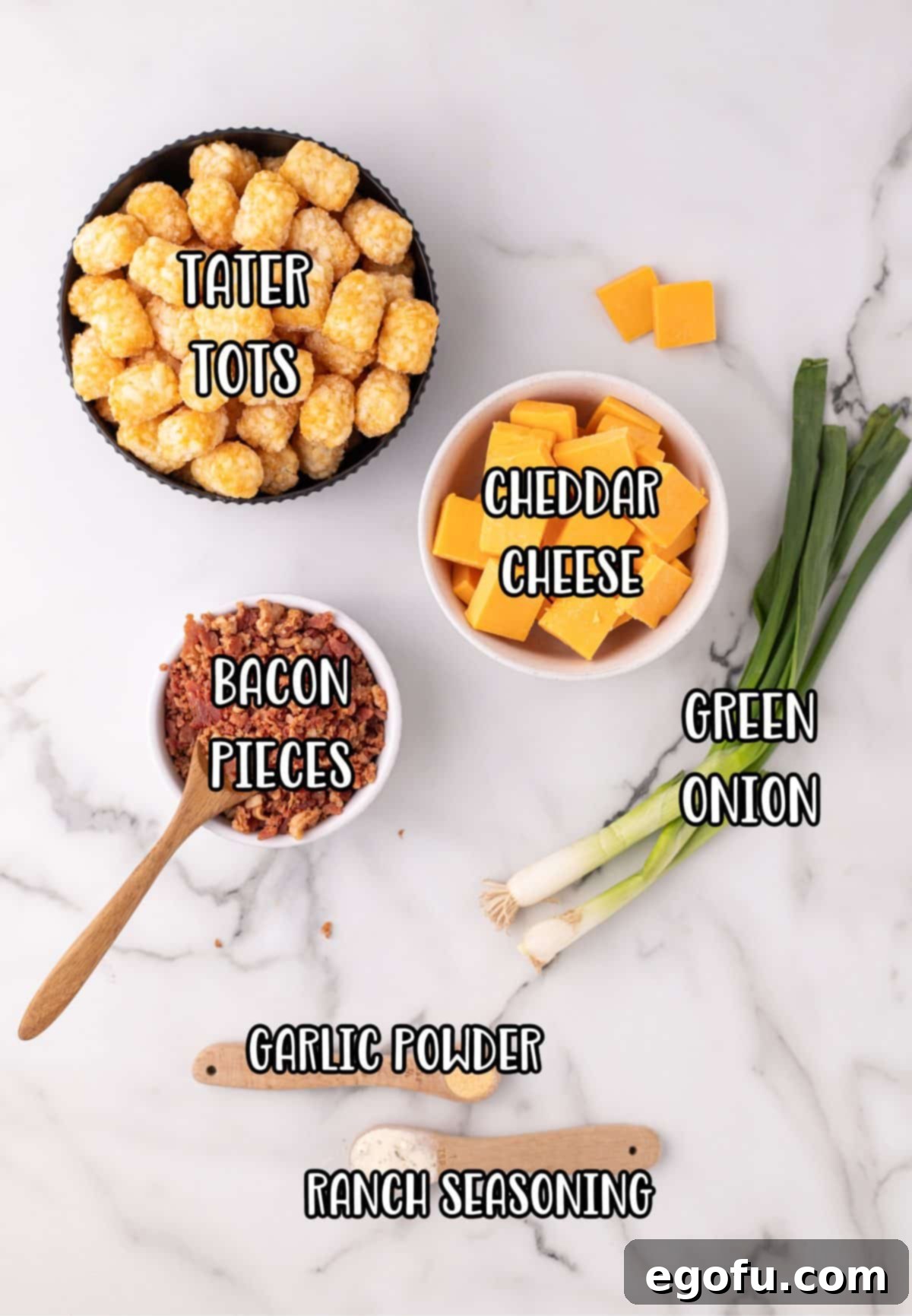 An array of fresh ingredients laid out: tater tots, cheddar cheese blocks, green onion, bacon pieces, garlic powder, ranch seasoning, and sour cream.