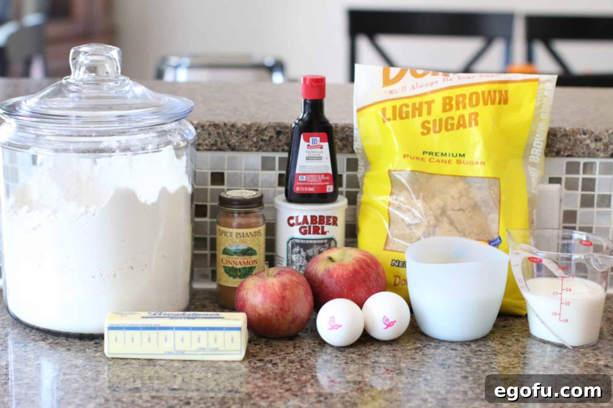 A flat lay of all ingredients for Apple Pie Bread: brown sugar, ground cinnamon, sugar, salted butter, eggs, vanilla extract, all-purpose flour, baking powder, milk, and fresh apples.