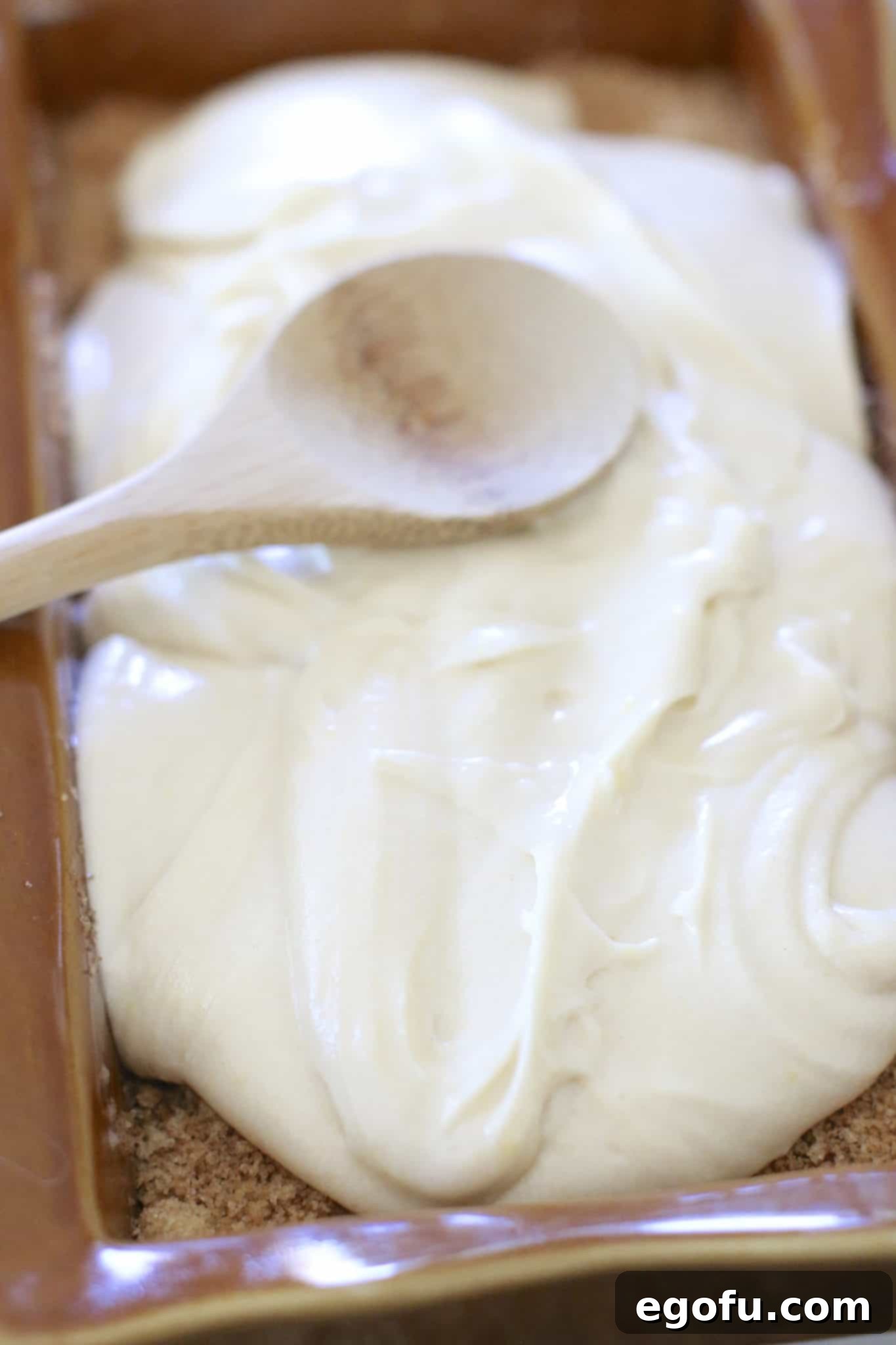 Final layer of apple bread batter spread on top of cinnamon sugar with a small wooden spoon.