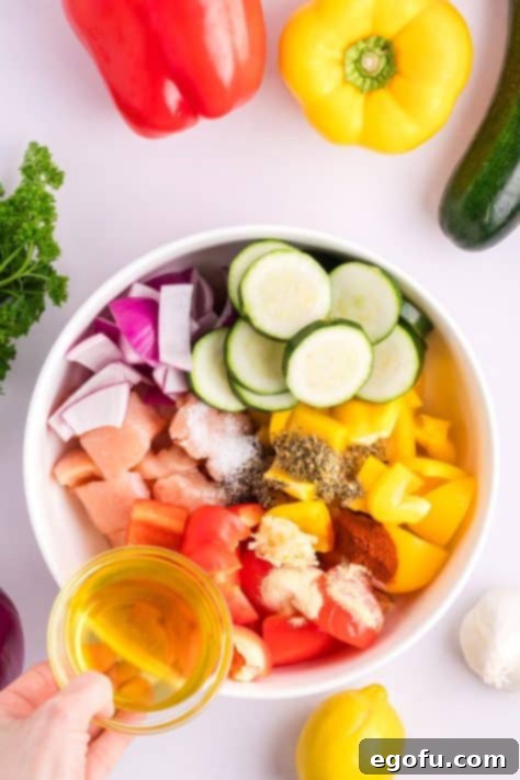 A bowl with chicken, zucchini, bell peppers, onion, olive oil, minced garlic, lemon juice, sweet paprika, Italian seasoning, kosher salt, black pepper, onion powder, and garlic powder.