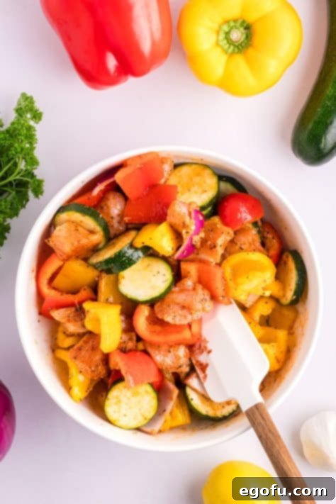 A bowl with chicken, zucchini, bell peppers, onion, olive oil, minced garlic, lemon juice, sweet paprika, Italian seasoning, kosher salt, black pepper, onion powder, and garlic powder being mixed together.