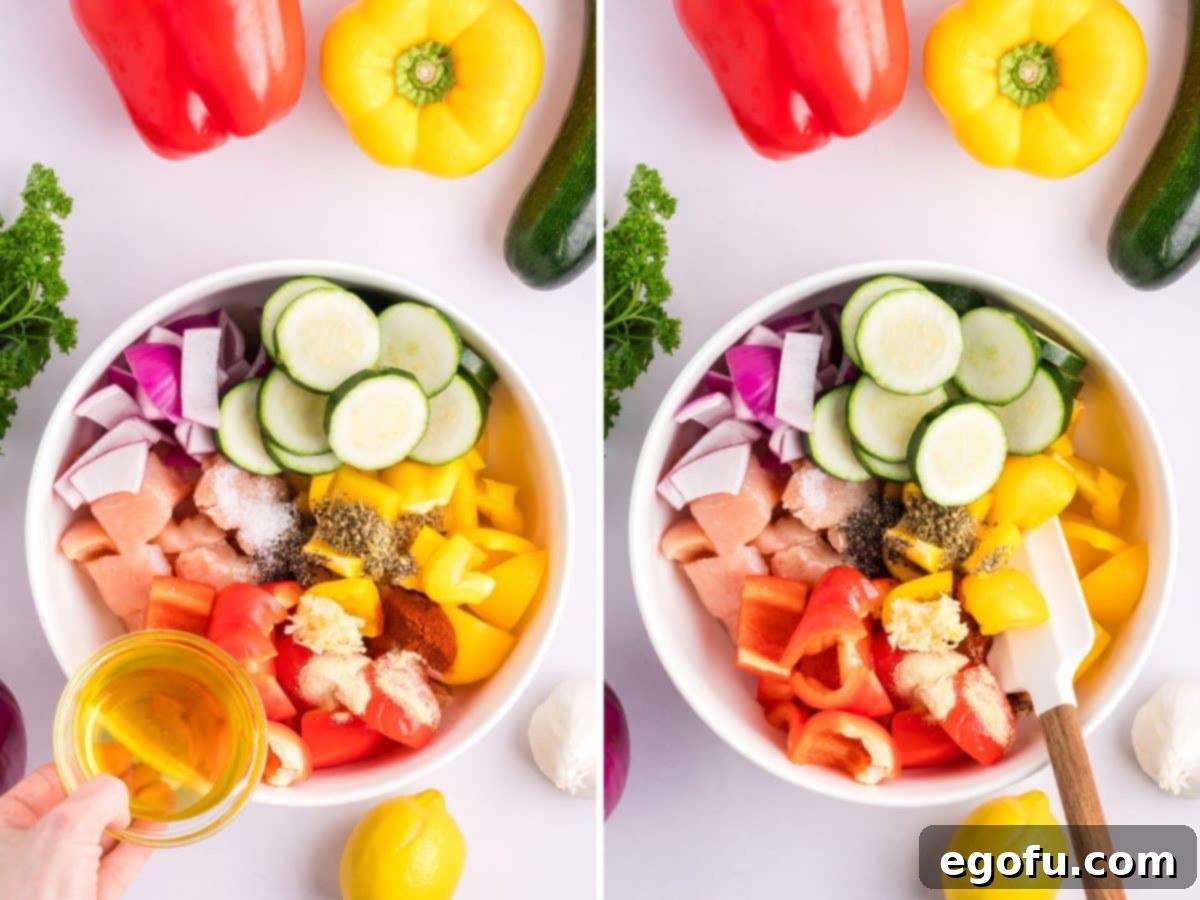 A large bowl containing cubed chicken, sliced zucchini, bell peppers, red onion, olive oil, minced garlic, lemon juice, paprika, Italian seasoning, kosher salt, black pepper, onion powder, and garlic powder, being mixed together to evenly coat the ingredients.