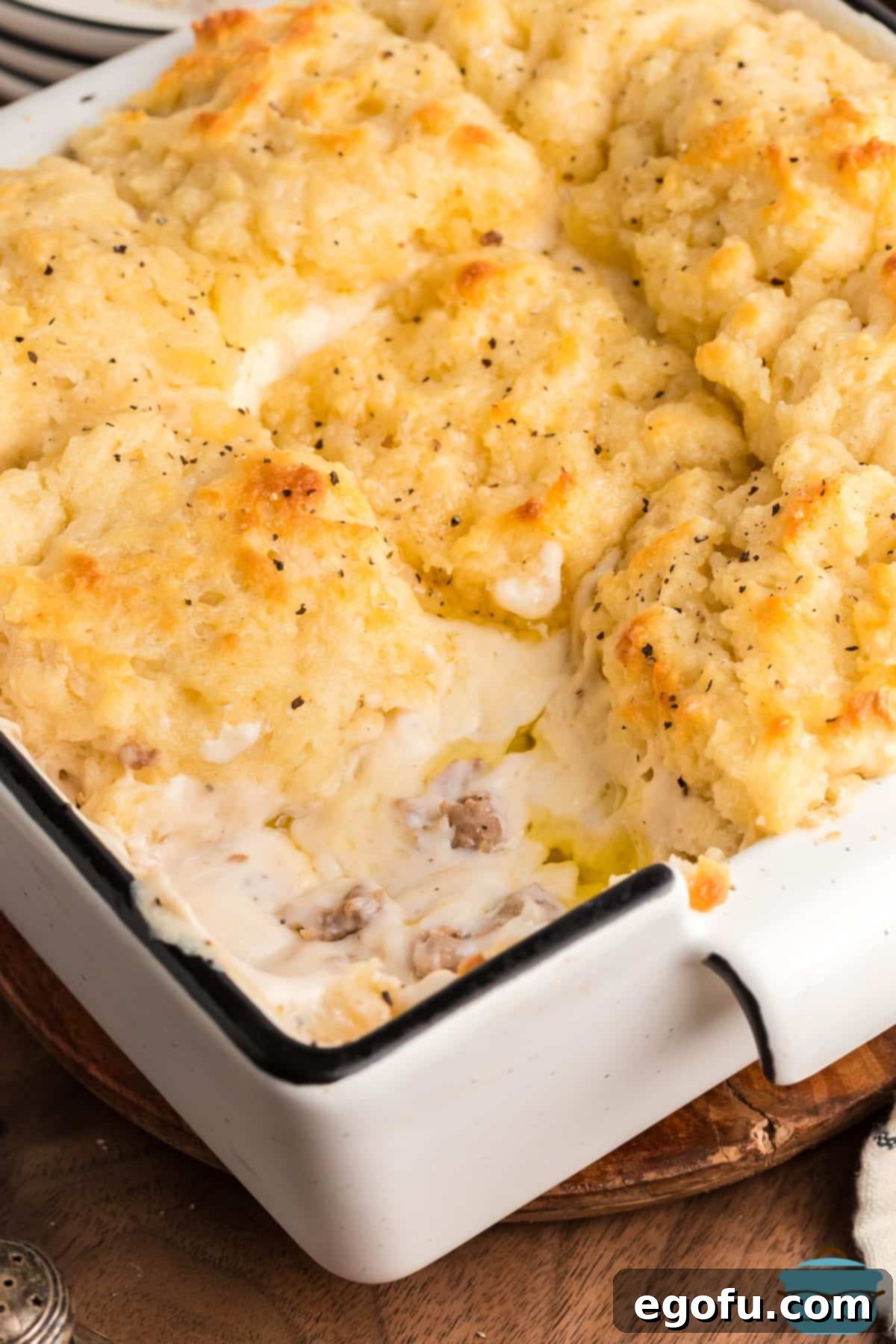 A baking dish with a Sausage Gravy Butter Swim Biscuit removed and the rest of the dish still full.