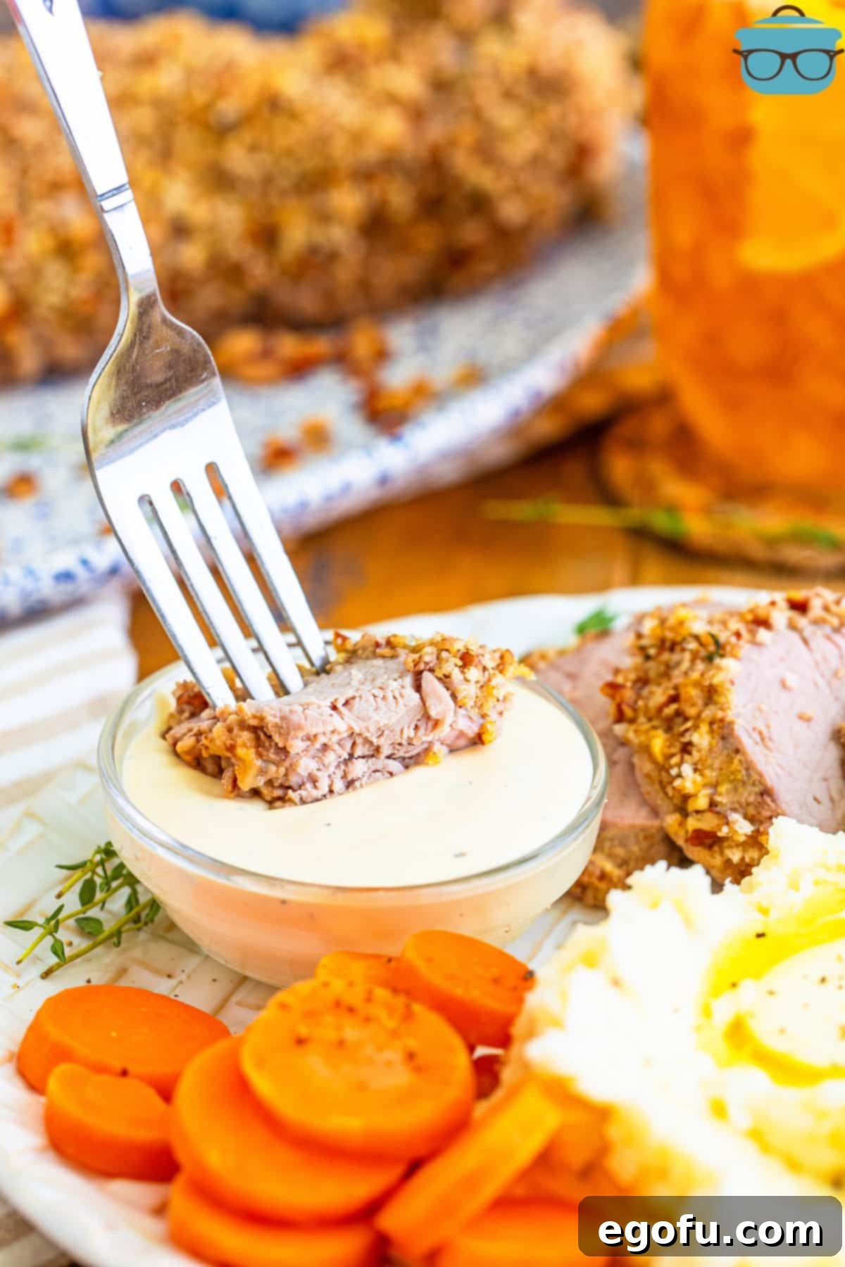 A fork dipping a slice of Pecan Crusted Pork Tenderloin in a homemade sauce.