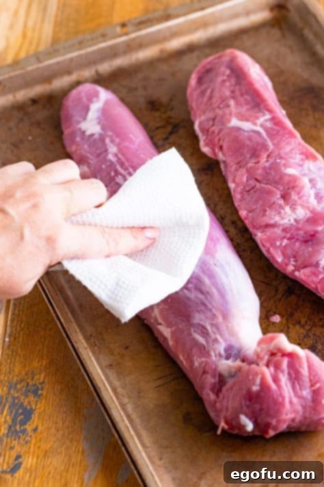 Hands using paper towels to pat pork tenderloins dry.