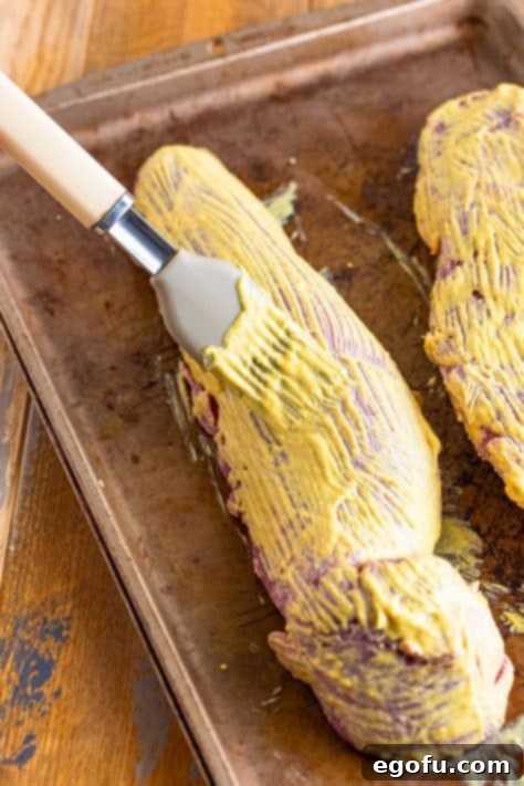 A pastry brush brushing the Dijon mustard over the pork tenderloin.