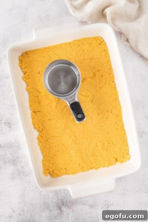 Lemon Oreo cookie crumb mixture being pressed on the bottom of a baking dish.