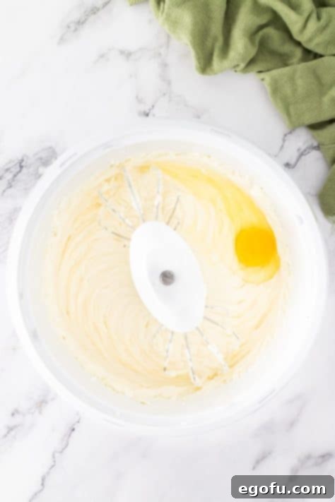 Eggs being added to the cheesecake mixture in a bowl.