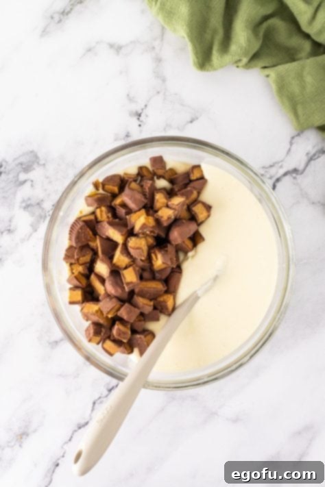 Peanut butter cups being folded into the cheesecake mixture.