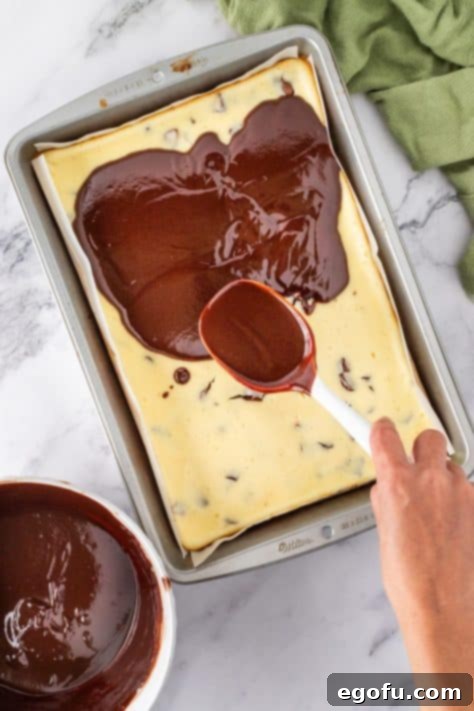Chocolate ganache layer being poured over the cheesecake layer.
