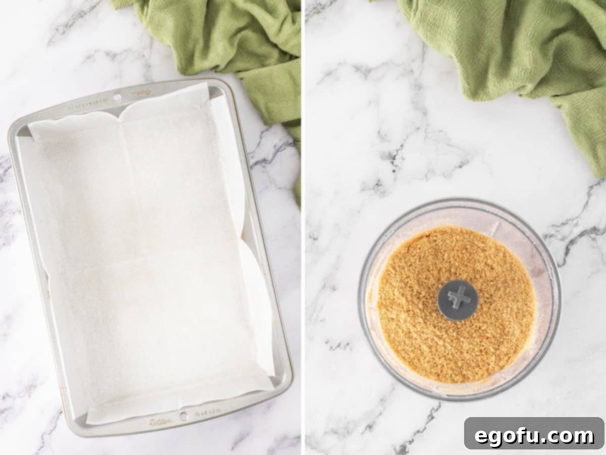 A baking dish lined with parchment paper and graham cracker crumbs in a food processor bowl.