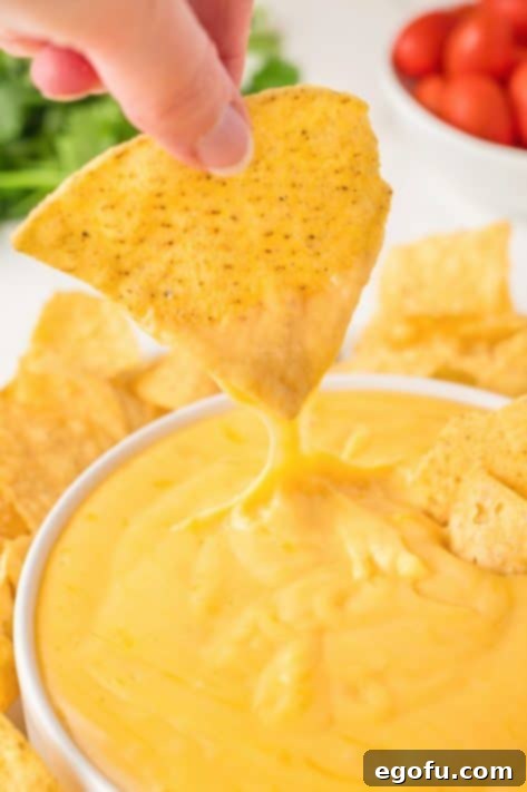 A chip being dipped into the finished, creamy Nacho Cheese Sauce, showing its perfect consistency.