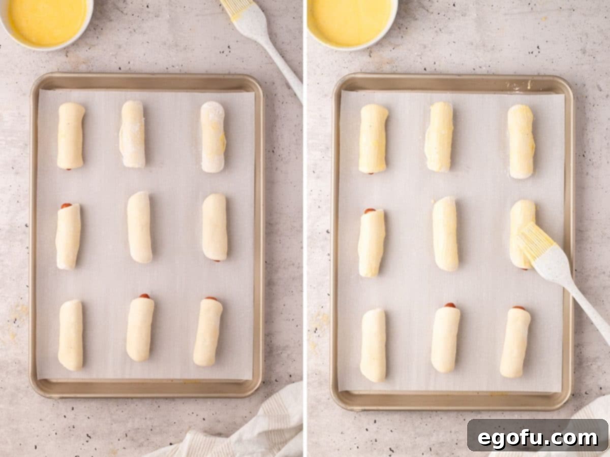 Hearty Texas Sausage Kolaches 8 Rolled up sausages in dough on a baking sheet, with an egg wash being brushed onto the dough.