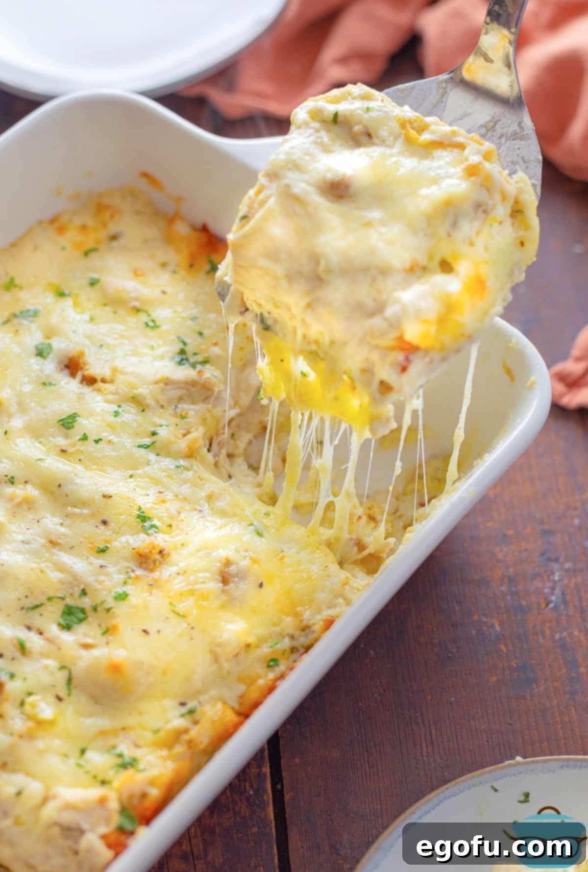 A serving utensil holding a scoop of White Chicken Enchilada Casserole, showcasing its creamy, cheesy layers.