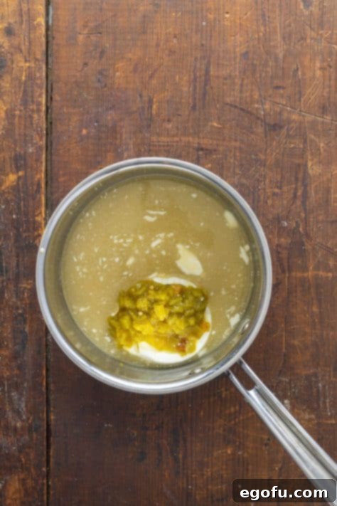 A skillet with chicken broth, sour cream, cream cheese and chiles being added to make the sauce.