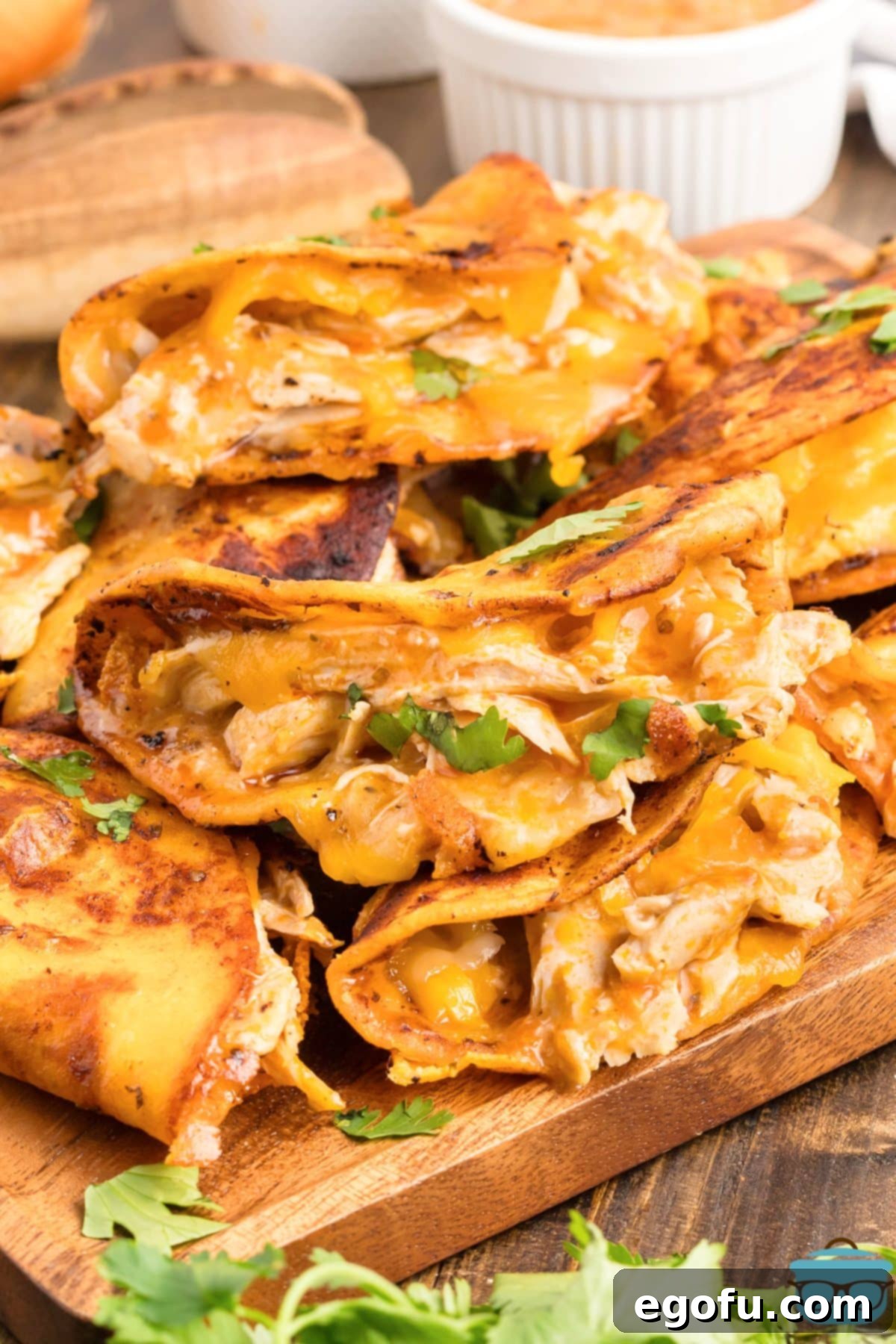 A small pile of Buffalo Chicken Tacos on a wooden board, garnished with fresh cilantro and a drizzle of dipping sauce.