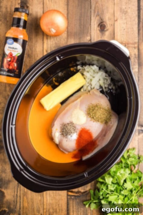 A crock pot with chicken, butter, wing sauce, chicken stock, onion, and dried seasonings.