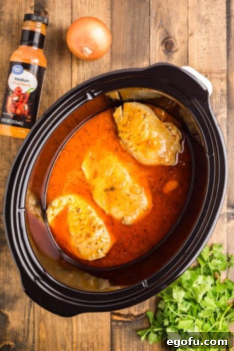 Chicken breasts in a seasoned buffalo sauce in a Crockpot.
