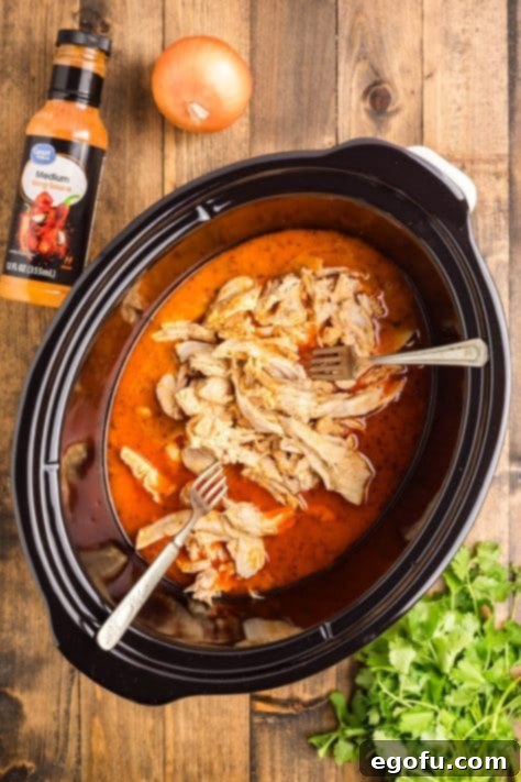 Chicken being shredded in a Crockpot with forks.