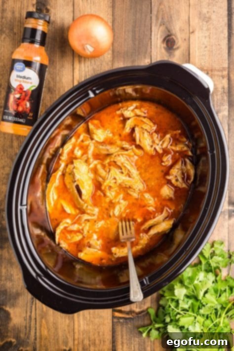 A Slow Cooker with shredded chicken in a buffalo sauce.