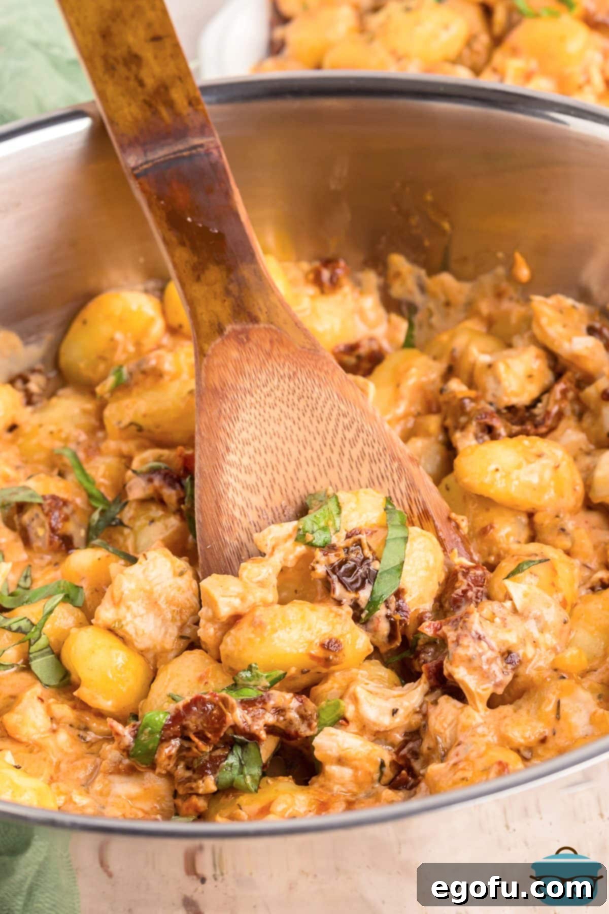 A wooden spoon in a pot of Marry Me Chicken Gnocchi, highlighting the creamy sauce and tender ingredients.