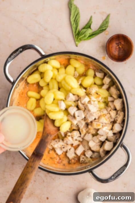 Gnocchi and pasta water being added to sauce ina skillet.