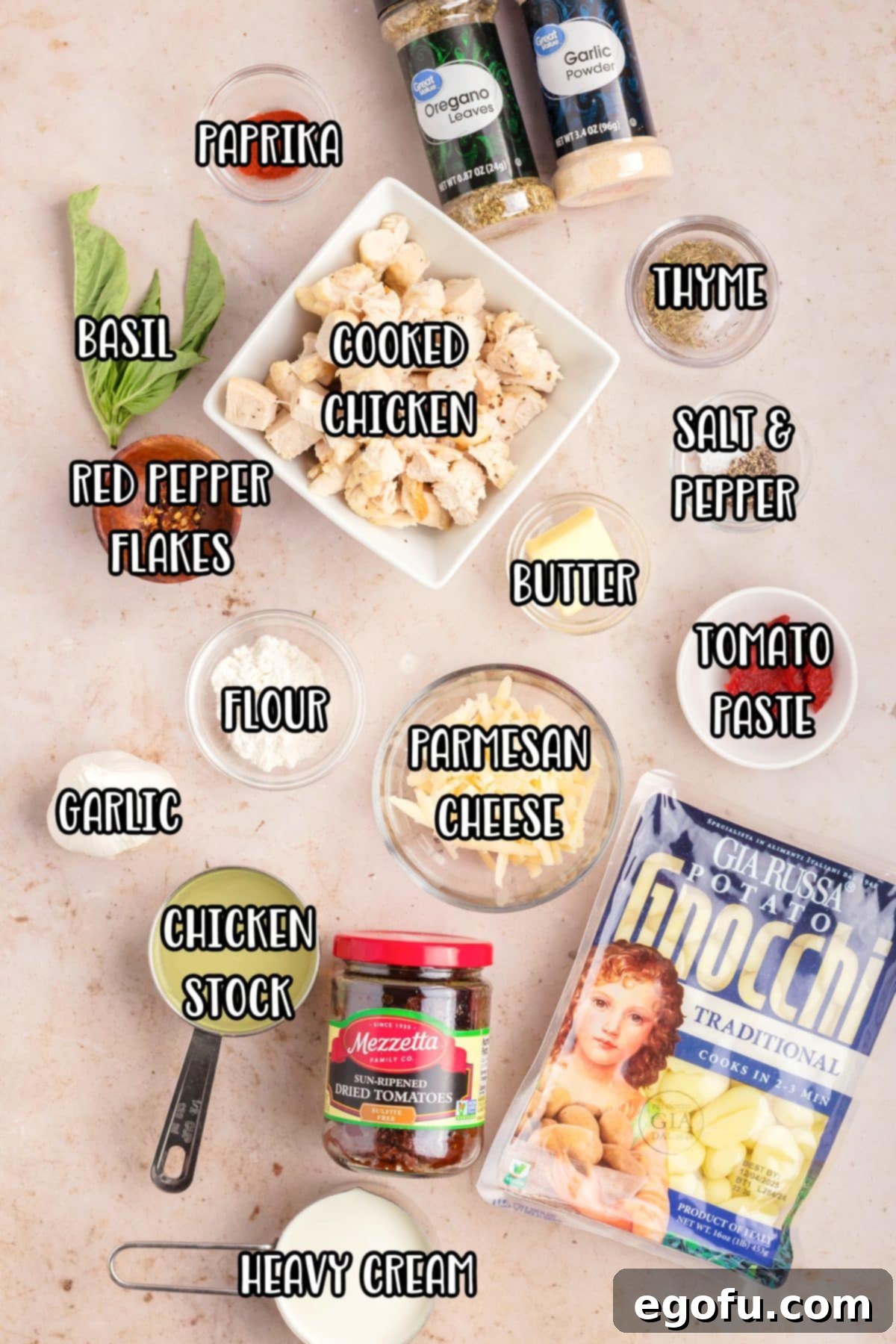 Various ingredients for Marry Me Chicken Gnocchi laid out: gnocchi, sundried tomatoes, cooked chicken, spices, butter, tomato paste, minced garlic, chicken stock, Parmesan cheese, heavy cream, and flour.