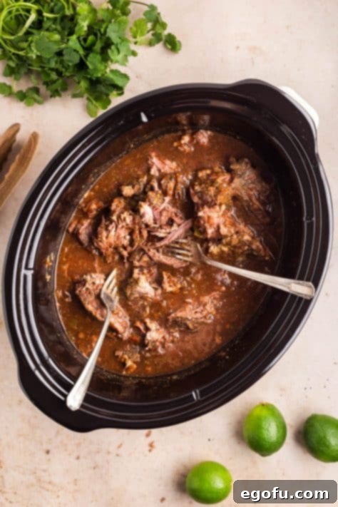 Two forks shredding meat in a Crock Pot.