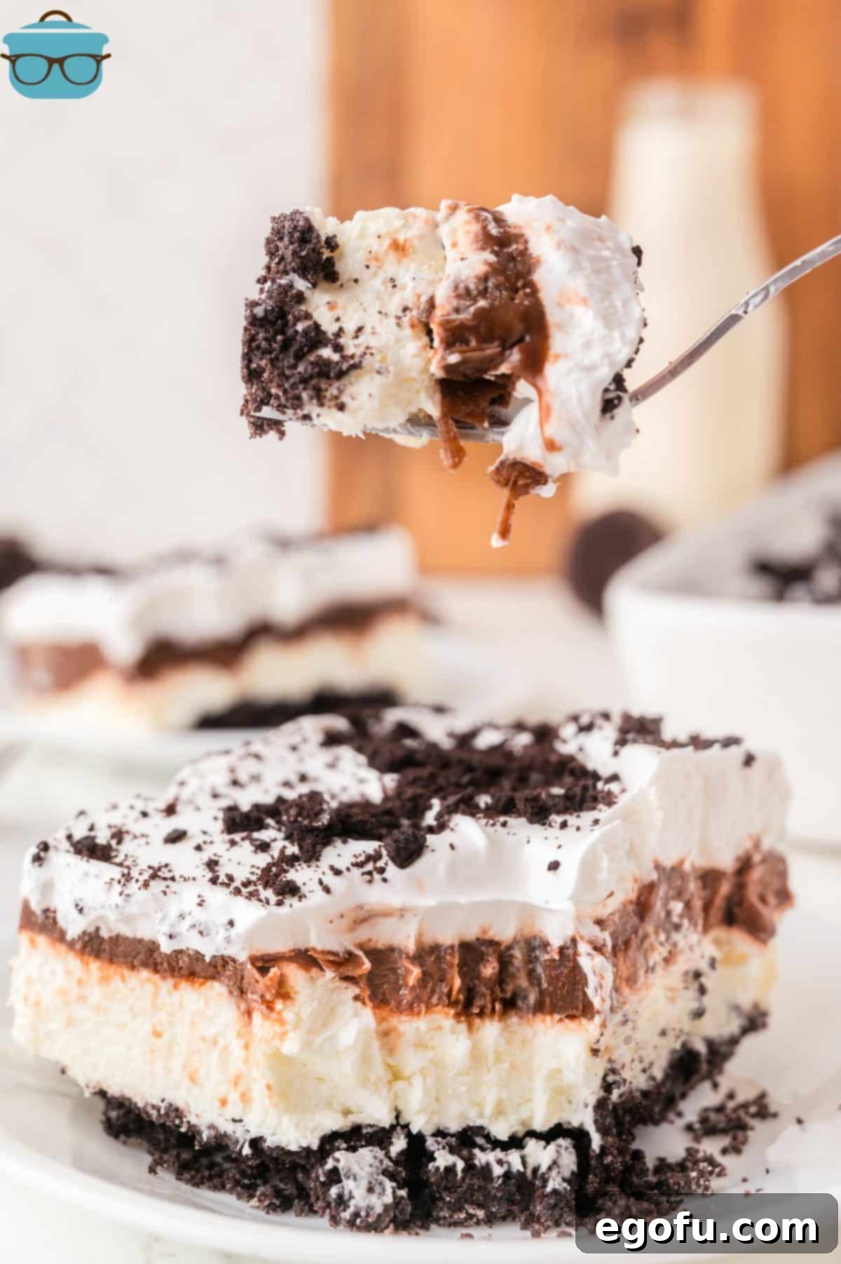 A fork holding a bite of Oreo No Bake Layered dessert above a slice of it.