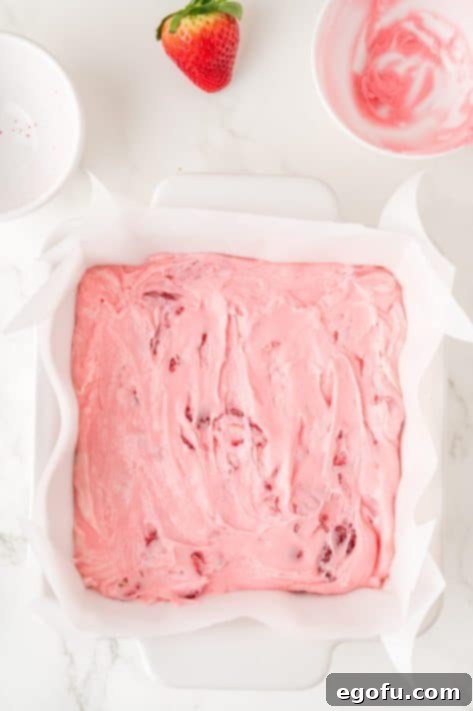 Strawberry fudge candy in a lined baking sheet.