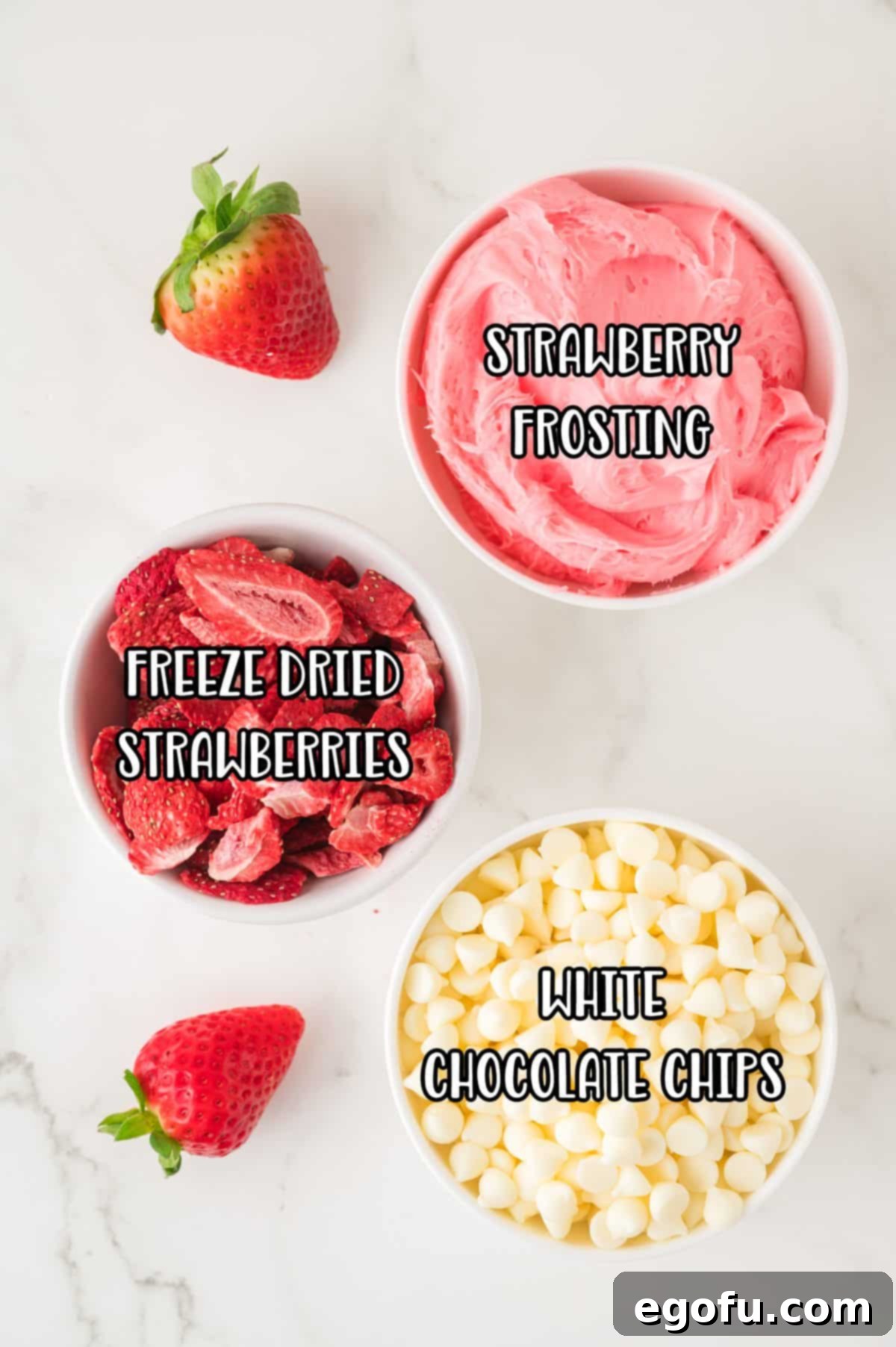 Strawberry frosting, white chocolate chips, and freeze dried strawberries, laid out as the three key ingredients.