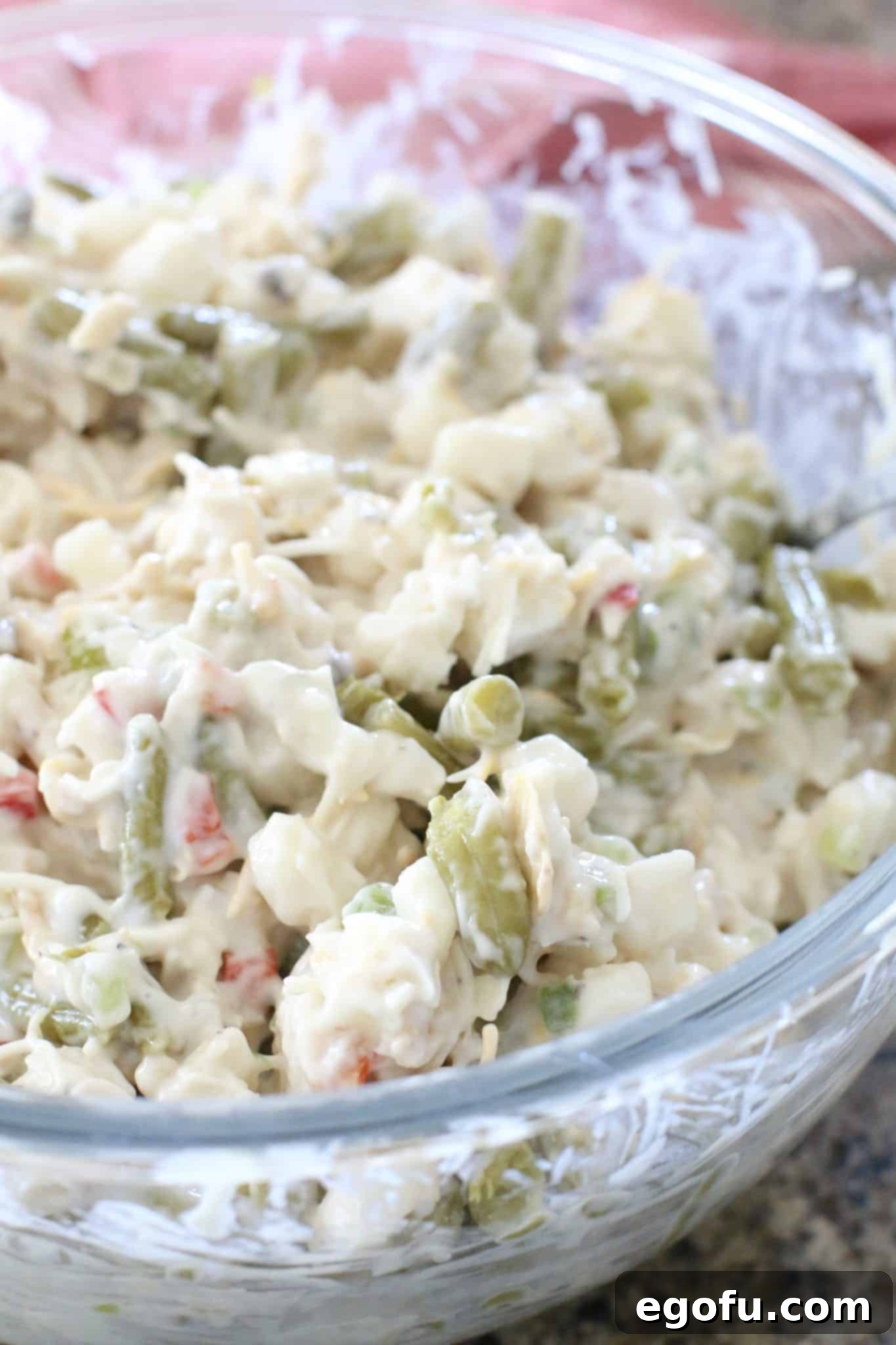 Homestyle Potato Green Bean Bake 5 A large glass mixing bowl filled with a creamy, uncooked mixture of condensed cream of mushroom soup, milk, garlic salt, frozen O'Brien potatoes, and drained green beans, all thoroughly mixed and ready for the next step.