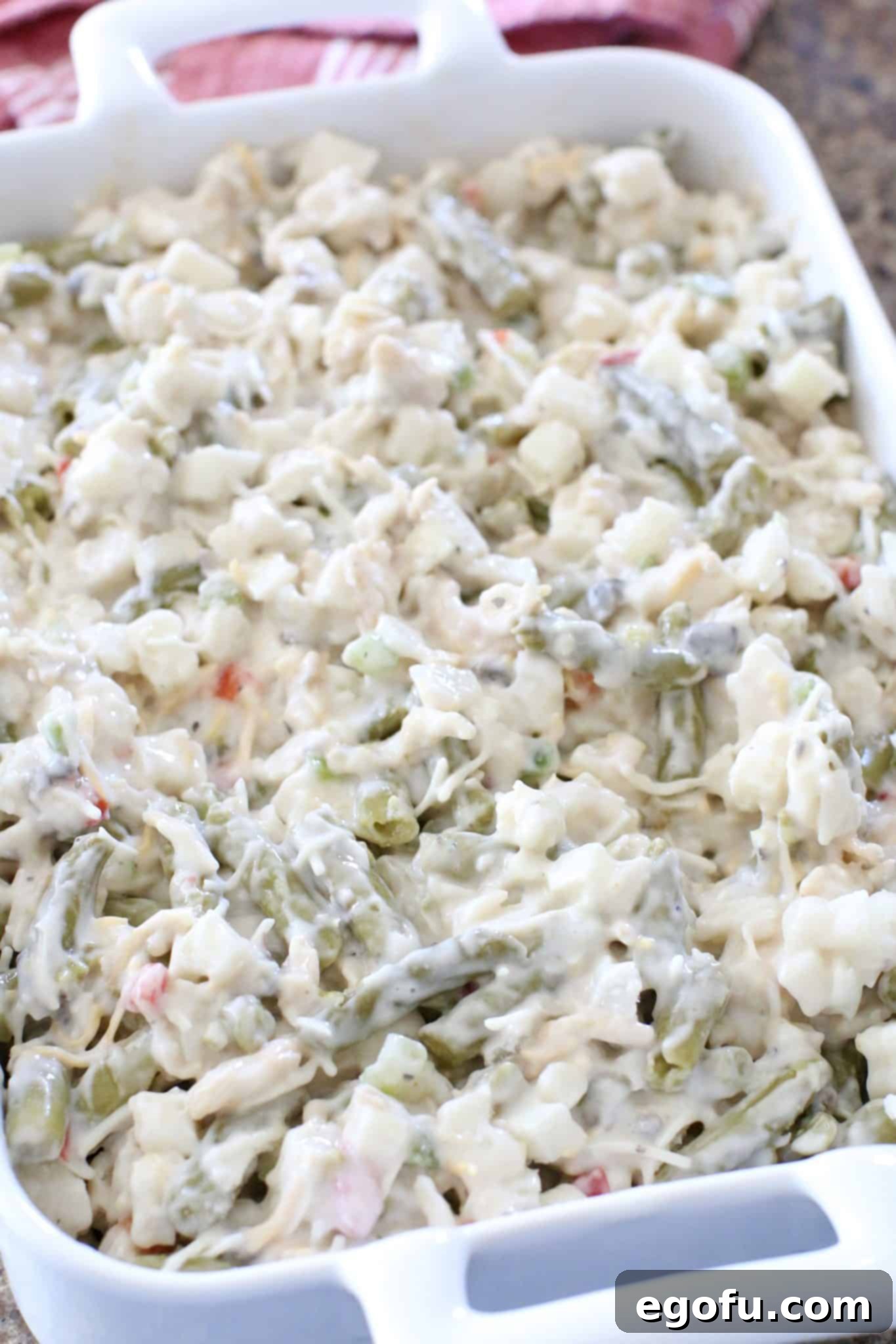 Homestyle Potato Green Bean Bake 6 Uncooked Tater Green Bean Casserole mixture spread out evenly in a rectangular white baking dish, prepared and ready to be placed in the oven for its first bake.
