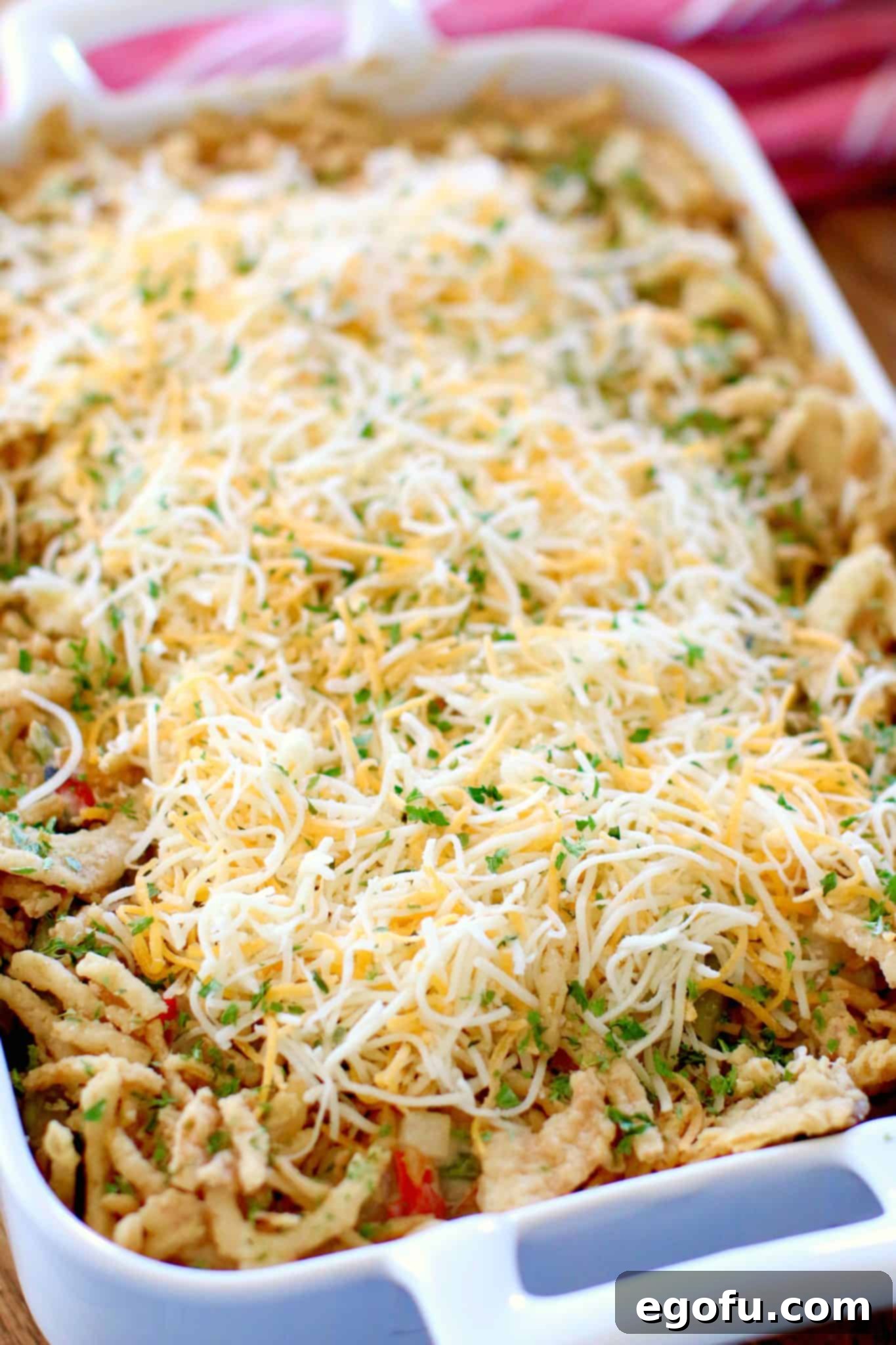 Homestyle Potato Green Bean Bake 7 Tater Green Bean Casserole in a white baking dish, freshly topped with a generous layer of shredded cheese and crispy fried onions, perfectly prepped for its final bake until golden and bubbly.