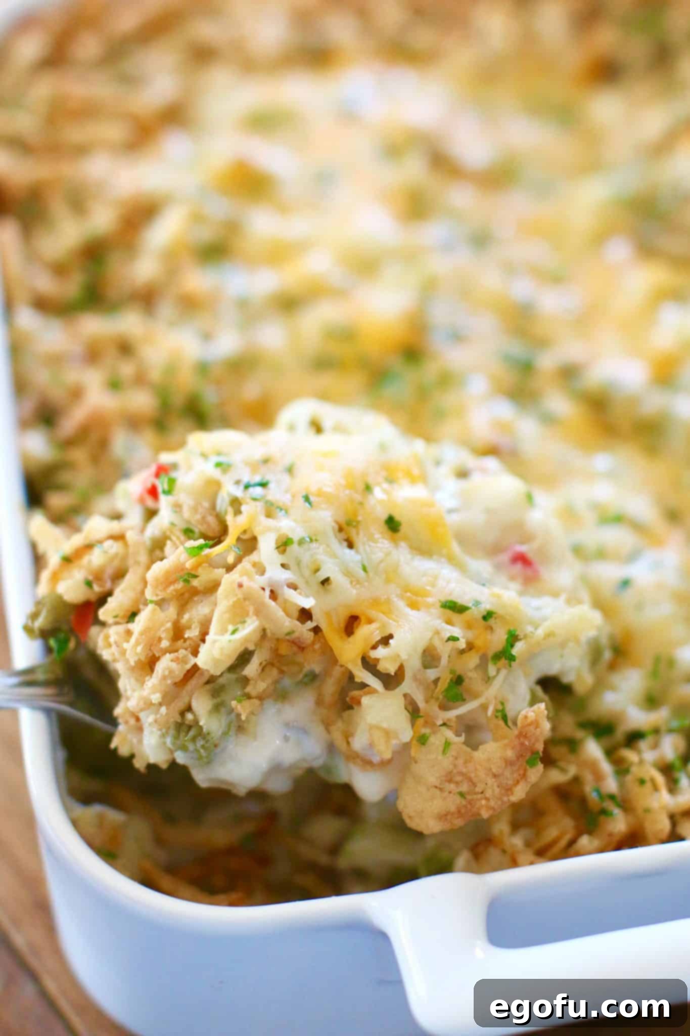 Homestyle Potato Green Bean Bake 8 A large silver serving spoon scooping a portion of the hot and bubbly Tater Green Bean Casserole from the white baking dish, revealing the creamy interior of green beans and potatoes.