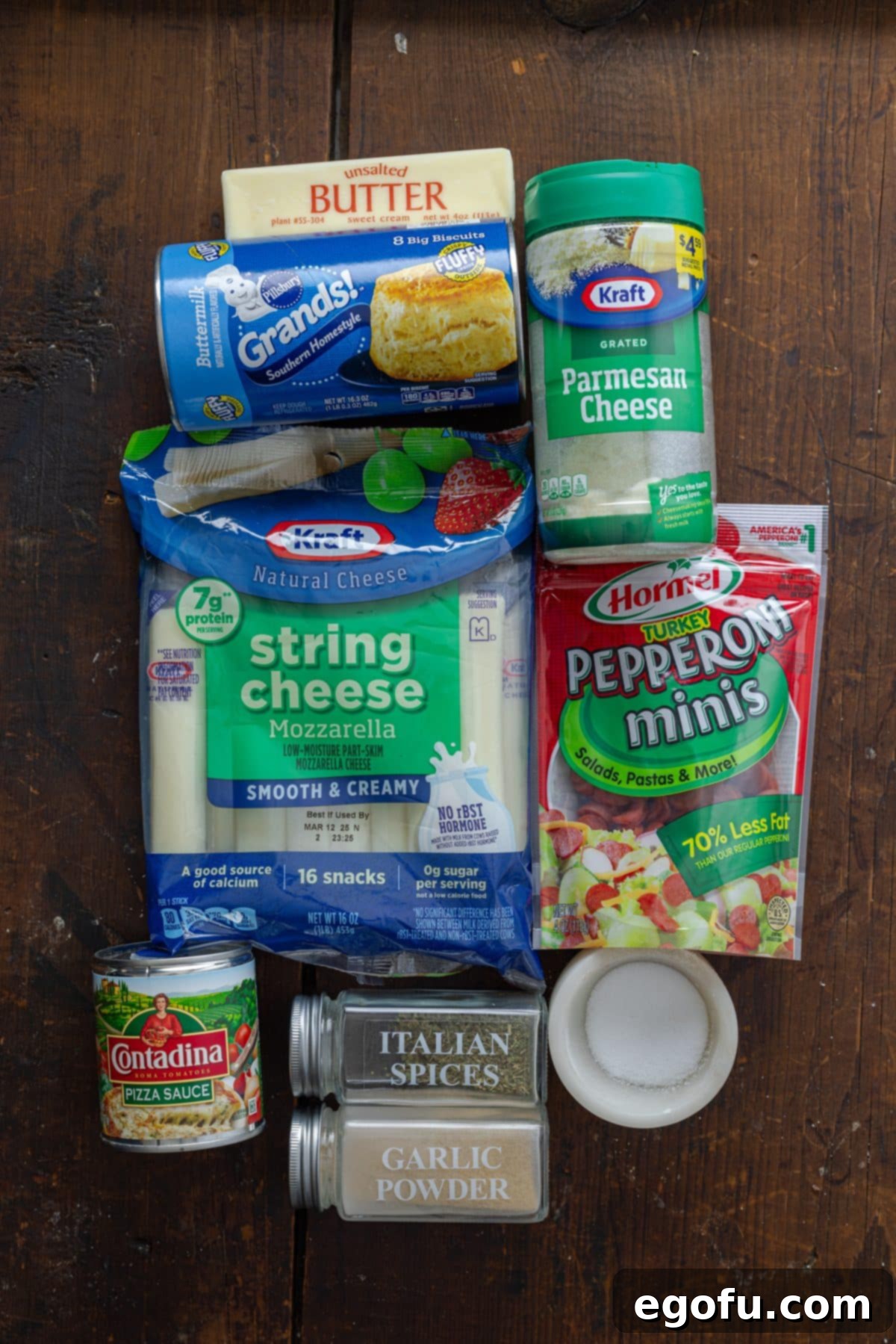 An array of ingredients for Air Fryer Pizza Bombs: canned biscuit dough, grated Parmesan cheese, pizza sauce, mini pepperonis, butter, Italian seasoning, garlic powder, string cheese, and dried parsley.