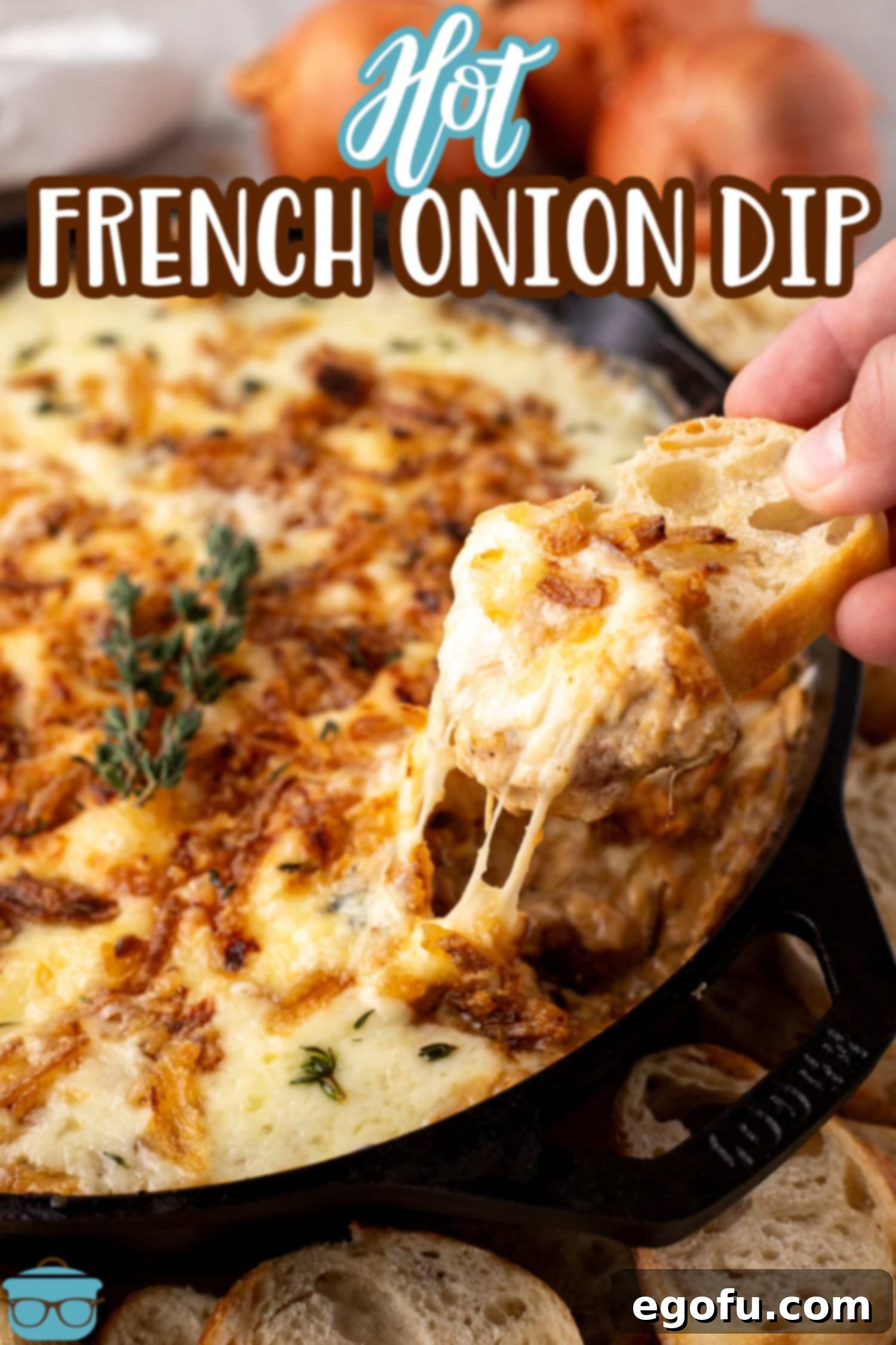 A hand dipping a cracker in a skillet full of cheesy, Hot French Onion Dip.