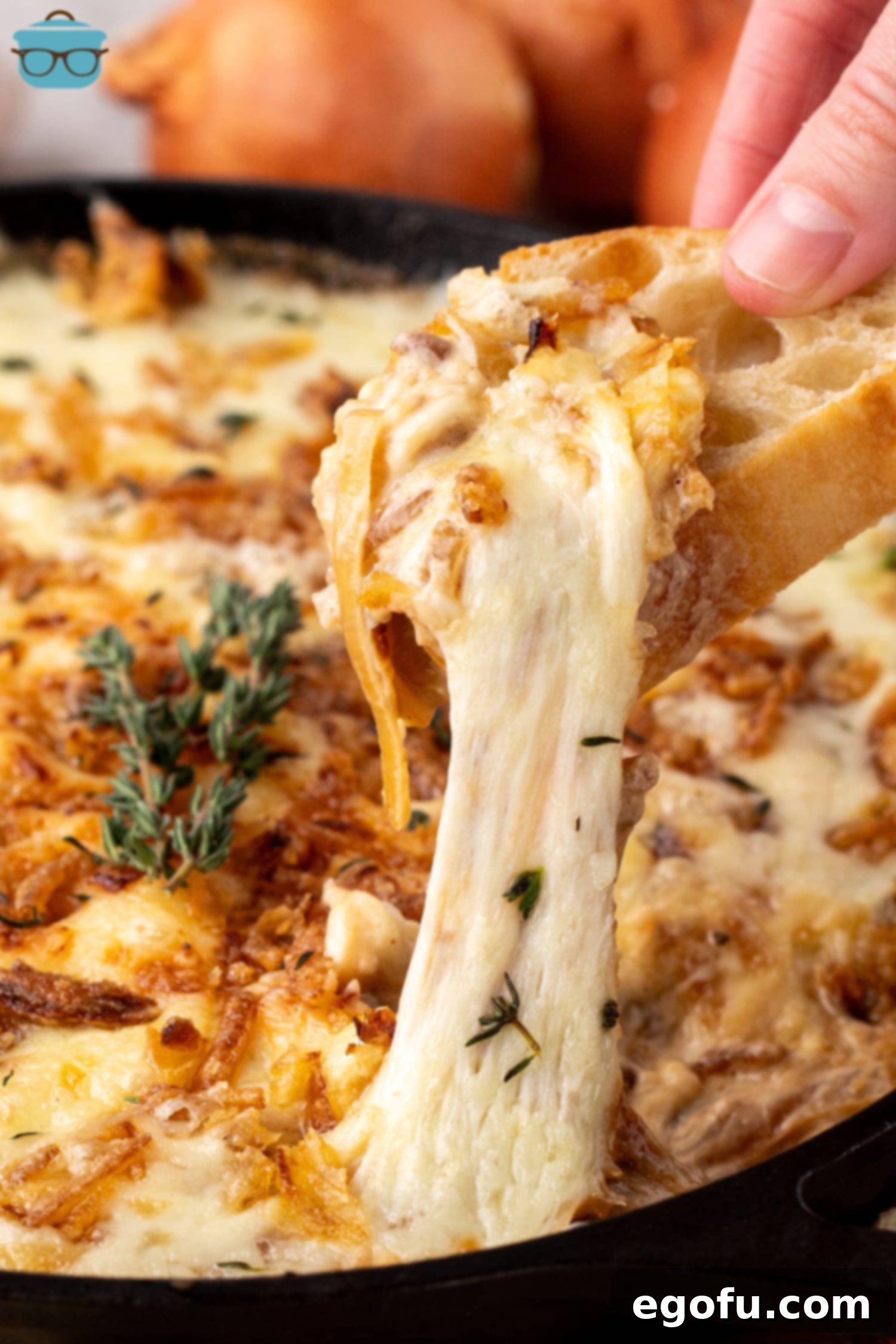 Some Hot French Onion Dip with melty cheese falling off a slice of baguette.